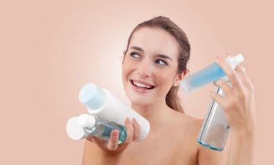 Smiling young woman holding various skincare bottles and bath products, including micellar water...