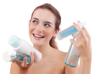 Smiling young woman holding various skincare bottles and bath products, including micellar water...