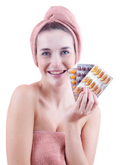 Smiling woman holding beauty and wellness supplements blister packs, with towel on head and body. Self care, health, daily beauty routine, clean skin and hygiene concept. Isolated on white background