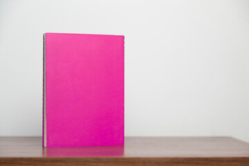 A pink book on a wooden table. Book concept. Knowledge concept. 
Space for text.