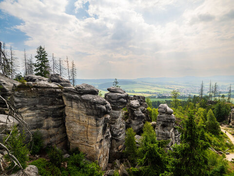 Landscape picture of sandstone formation of stone city in Ostas in Czech Republic. Cloudy day, grey and brown tall rock formations, evergreen spruce trees, hills in distant.