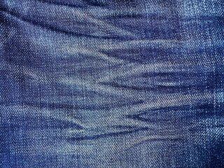 Macro close-up of faded blue denim fabric with whisker creases, detailed jean texture ideal for...