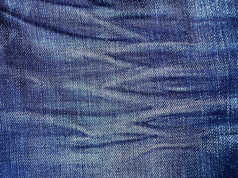 Macro close-up of faded blue denim fabric with whisker creases, detailed jean texture ideal for backgrounds and fashion design mockups. - Powered by Adobe