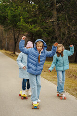Teen girls ride skateboards on city path in winter autumn park. Jackets and jeans reflect urban...
