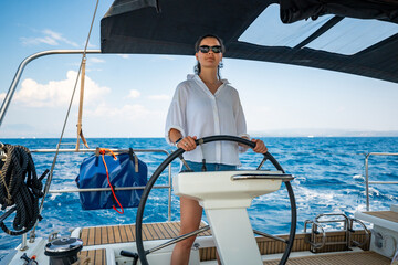 Young woman steering a sailing yacht near Croatia, confidently standing at the helm. Female...