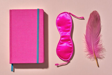 Pink journal, sleep mask, and feather on pastel background, promoting relaxation, mindfulness, and self care in minimal, tactile wellness display
