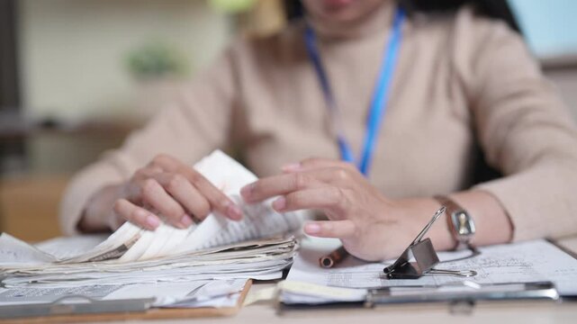 A woman is sitting at a desk with a stack of money in her hand. She is looking at the money and she is counting it