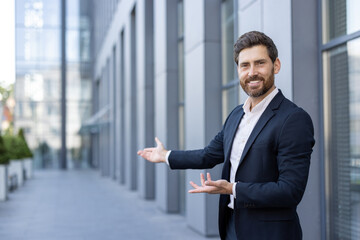 A businessman in a suit gestures with both hands, welcoming or presenting something in front of a...