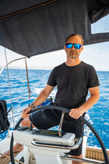 Man standing at the helm of a sailing yacht near Croatia, steering the boat through open water....