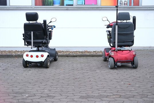 Konzept Alter, &Uuml;beralterung, Mobilit&auml;t und Gesellschaft im demografischen Wandel: Zwei Elektromobile mit Einkaufskorb parken nebeneinander vor einem Gesch&auml;ft, viel Copyspace