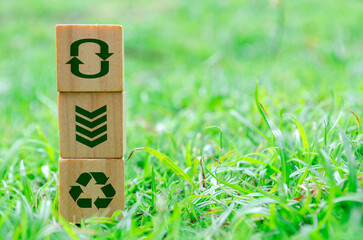 Wooden cube stack with recycle, reuse, reduce icons on green grass. Environmental concept