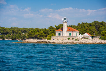 Stone lighthouse with red roof on the rocky coast of Hvar Island, Croatia, surrounded by pine trees...