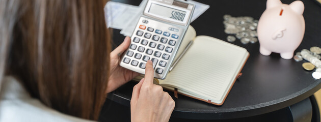 Young woman saving money monthly expenses putting coin in to piggy bank on the table.