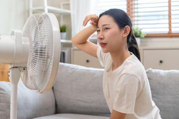 Suffer summer heat wave stroke, hot weather, tired asian young woman sitting on couch in living...