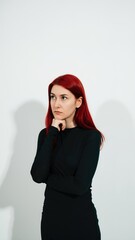 Red-haired woman stands in front of a white wall and thinks.