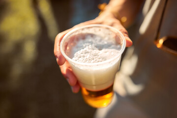 Person holding beer cup outdoors on a sunny day.