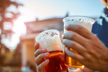 Person holding beer cup outdoors on a sunny day.