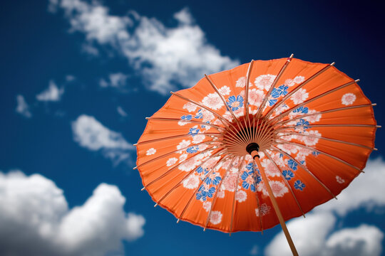 Orange parasol with flower decorations open under a blue sky with some white clouds, providing shade and protection from the sun during a sunny day
