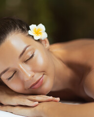 Beautiful Woman Resting on Spa Table with Glowing Skin and Tropical Flower