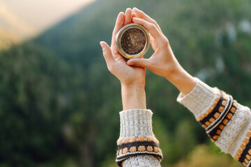 Close up of young female traveler hands with yellow backpack holding compass against mountain...