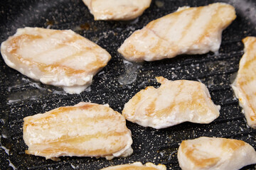 Grilled chicken fillets sizzling in a frying pan, showcasing golden-brown grill marks, surrounded...