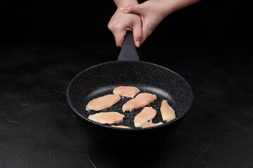 Cooking chicken fillets in a non-stick frying pan, with a hand holding the handle, showcasing the...