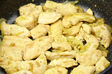 Sauteed chicken pieces seasoned with spices, cooking in a frying pan, surrounded by golden onions, showcasing a delicious meal preparation process in a kitchen setting