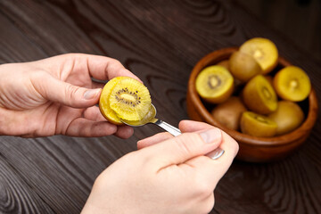 Hands holding a spoonful of sliced yellow kiwi fruit, showcasing its unique texture and color, with...
