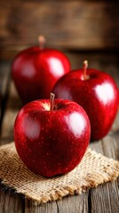 Three juicy red apples resting on burlap and wooden table