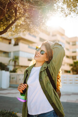 Cheerful woman with curly hair and sunglasses enjoys a sunny day on an alley with palm trees. A...