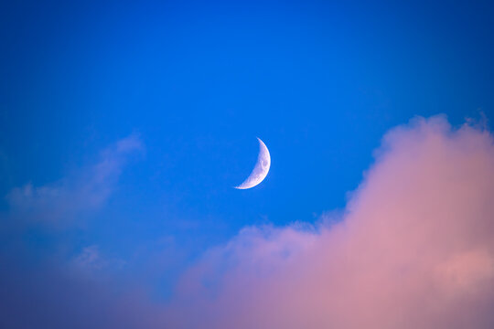 There is a white crescent moon and red clouds in the dark(deep) blue sky.