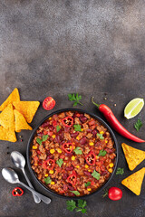 Chili con carne with fresh herbs and nachos chips on a gray background. Top view. Copy space. Mexican cuisine. 