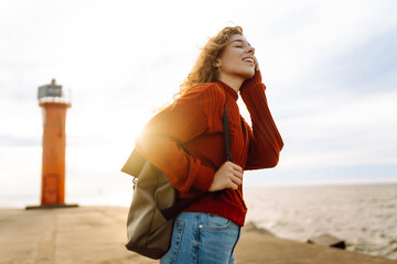 Portrait of beautiful woman on pier admiring seascape with lighthouse in background. Sweet woman...