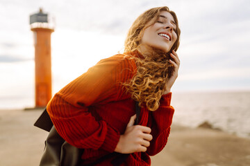 Portrait of beautiful woman on pier admiring seascape with lighthouse in background. Sweet woman...