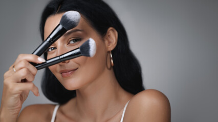 Smiling Woman Holding Makeup Brushes in Front of Her Face 