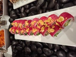 Vibrant Pink Sushi Rolls Topped with Crunchy Garnish on a White Platter