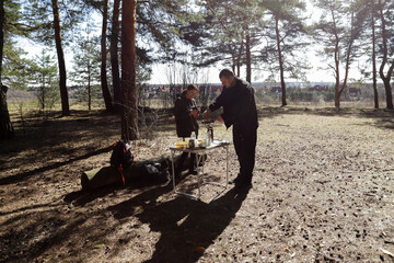a man prepares food and a woman enjoys a hot beverage, showcasing the joy of slow living and disconnecting in the forest