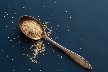 Ornate wooden spoon filled with quinoa grains on deep blue backdrop, showcasing texture, nutrition, and artisanal culinary elements