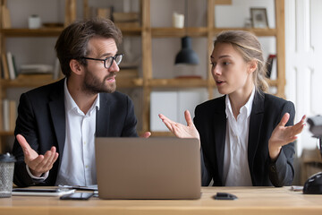Two business people gesturing and discussing issues near a laptop on an office desk