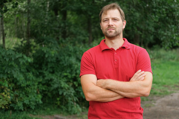 Portrait of handsome young man in a red t-shirt outdoors. Male with fair hair and beard feel happy,...
