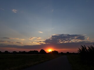 Stunning sunset over rural landscape with the sun setting behind soft clouds, casting warm golden...