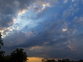 Evening countryside view with a striking sunset and storm clouds overhead, trees casting shadows...