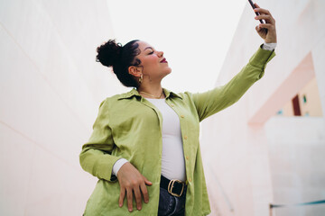 Young woman confidently takes a selfie, capturing moment with her smartphone. Female looks focused,...