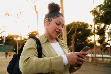 Latina Woman checks notifications on her smartphone application while walking outdoors. Using 5G...