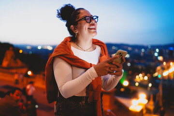 Smiling while holding her smartphone, young Latina woman stays connected in digital world. City...