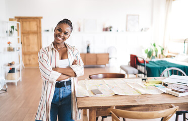 Confident smiling young woman posing near planning desk with large city map, fully prepared for...