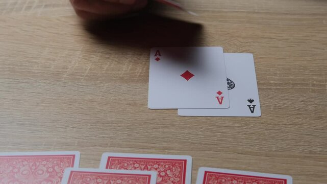 Close-up of a hand revealing four aces during a card game on a wooden table in a cozy environment