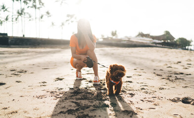 Brunette woman in orange sportswear performs yoga pose on sandy shore, illustrating harmony between...