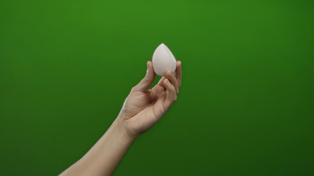 Man holding egg-shaped object against green background, hand poised elegantly, displaying precision and focus, isolated on vibrant surface in minimalist setting.