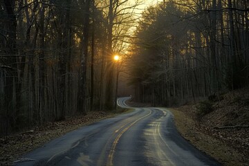 Sun setting behind trees illuminating winding road through forest creating a scenic drive